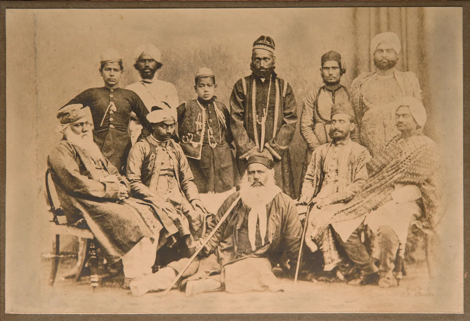 Sir Syed Ahmed Khan and others Photographed by J.H.Clarke Standing L-R Hamid ( son) Servant, Mahmood ( Son) Zainul Abideen, Mirza Bundo, Seated L – R Imdad Ali, Raja Jai Krishen Da…